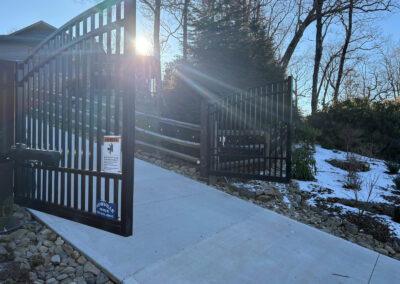 Arched black double swing driveway gate with its gate operator and safety warning sign
