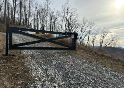 Black crossbuck swing gate with its gate operator across a gravel mountain driveway