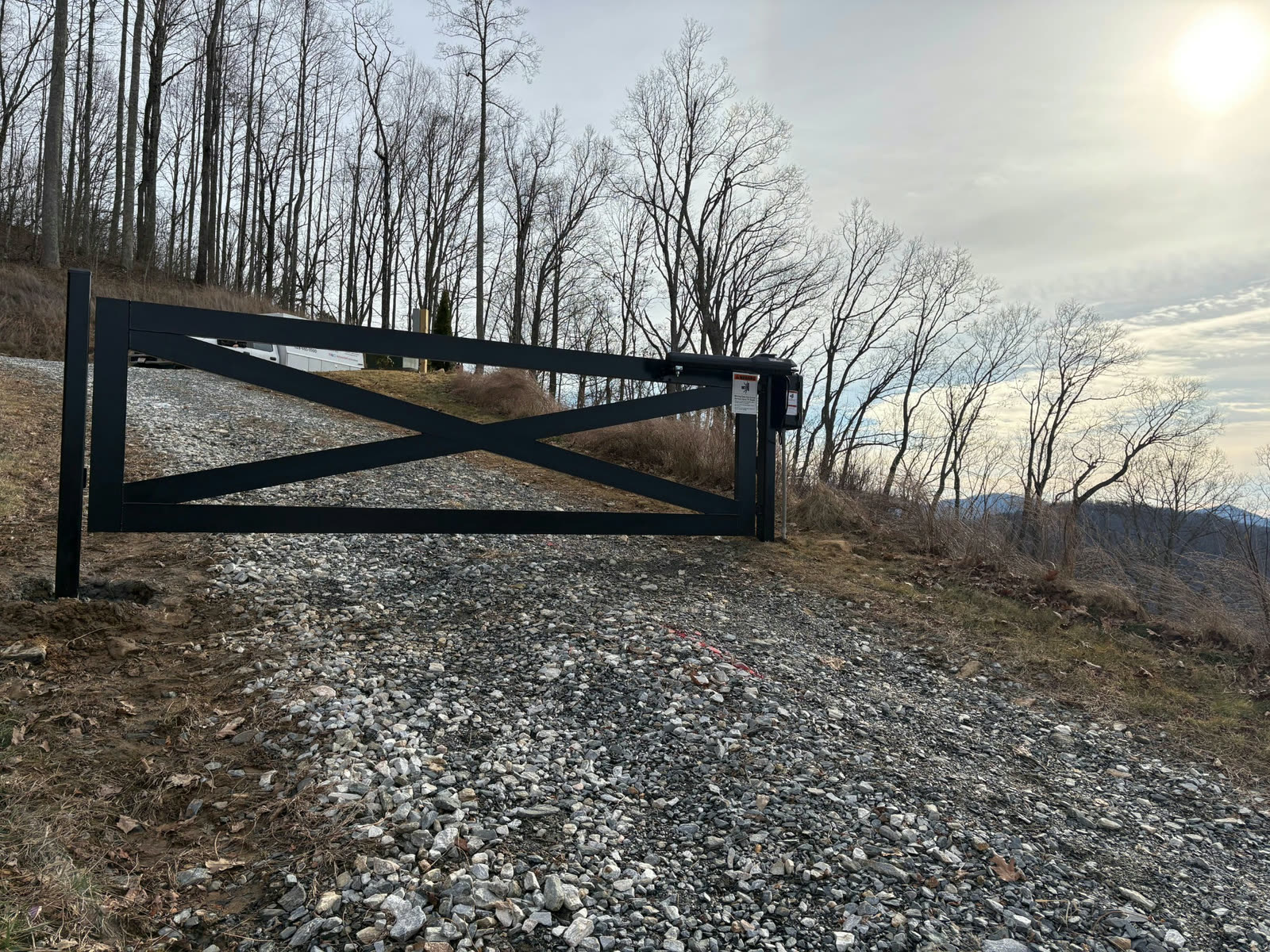 Black crossbuck swing gate with its gate operator, mountains behind