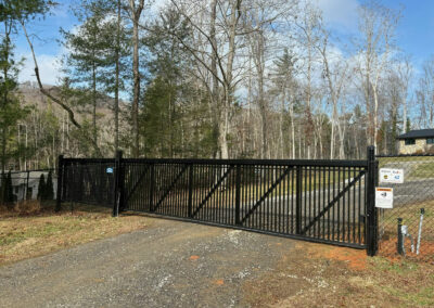 Black automatic slide gate across a gravel drive, between chain link fence